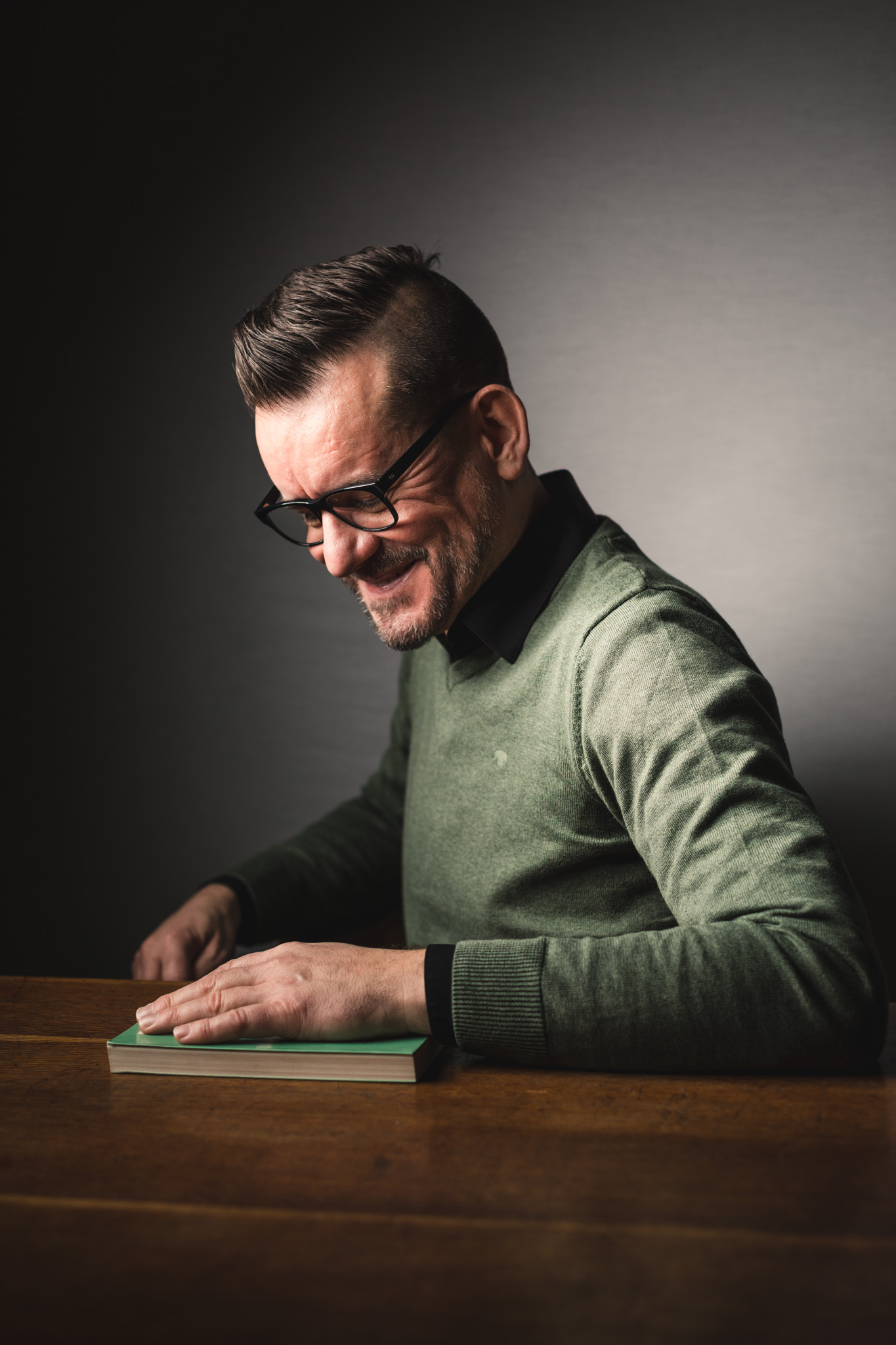 Jeugdauteur Bart Moeyaert zit lachend aan tafel. Voor hem ligt een boek op tafel, waarop zijn linkerhand rust.