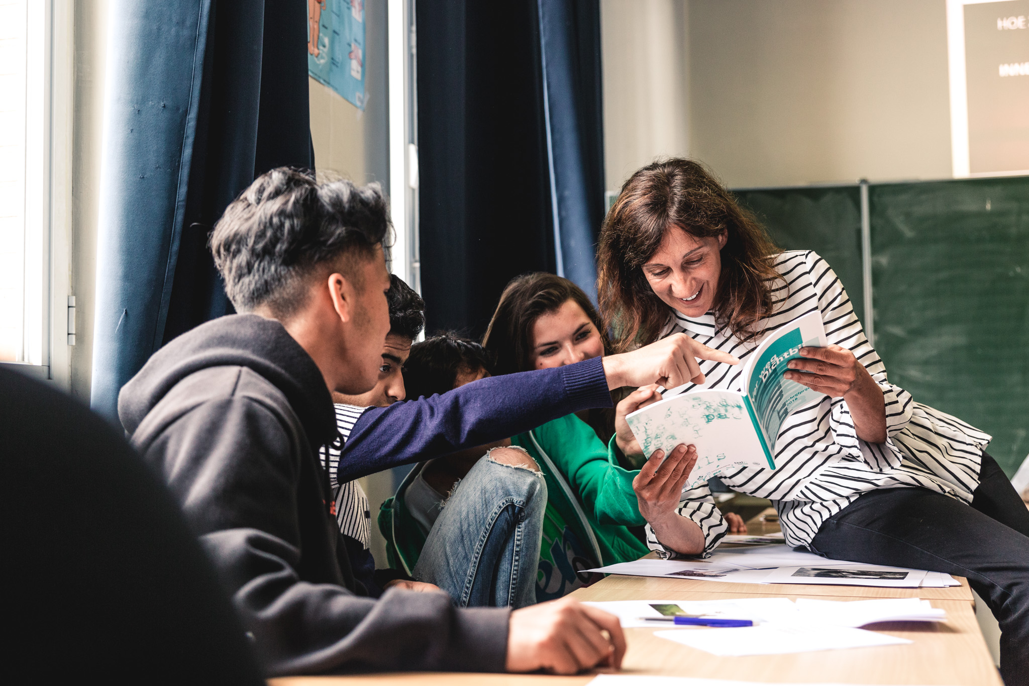 lachende leerlingen zitten aan hun schoolbank en kijken samen met een jeugdauteur in een boek