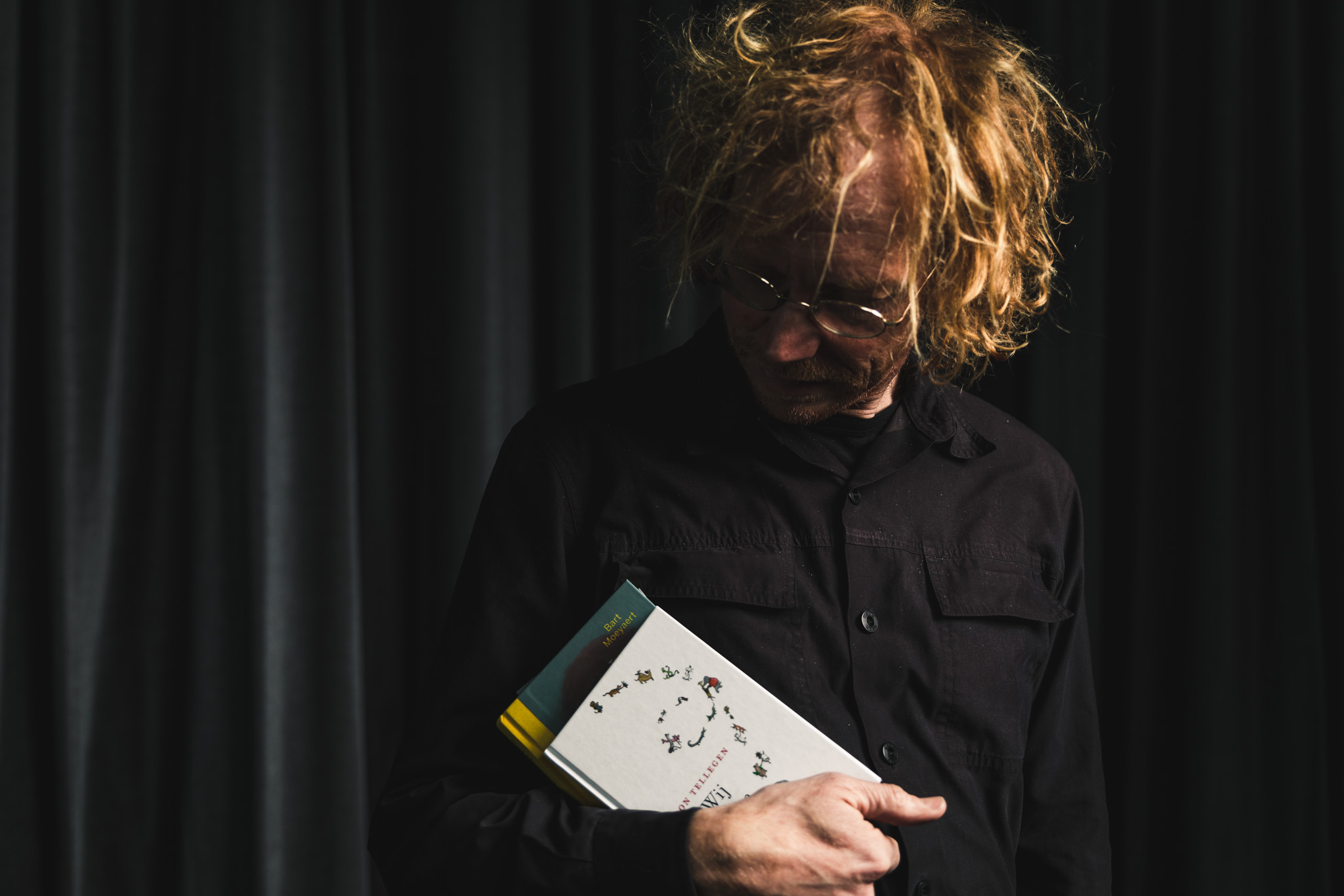 portret van Hendrik Vos, die twee boeken in zijn rechterarm vasthoudt. Hij kijkt naar de boeken. Op de achtergrond hangt een donkergrijs fluwelen gordijn.