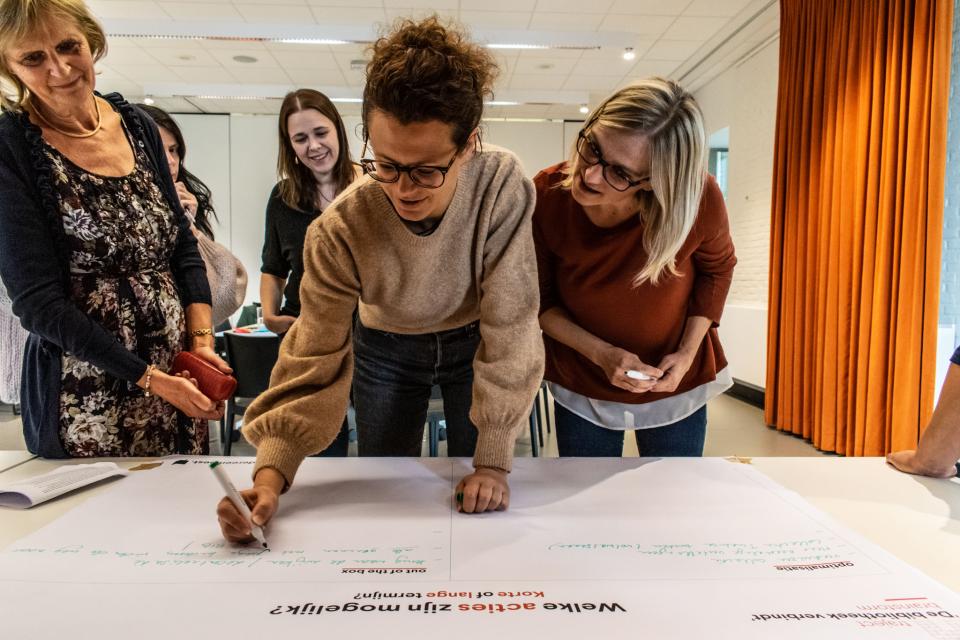 Bibmedewerkers schrijven acties rond meertaligheid neer op een groot blad tijdens een workshop in de bibliotheek.